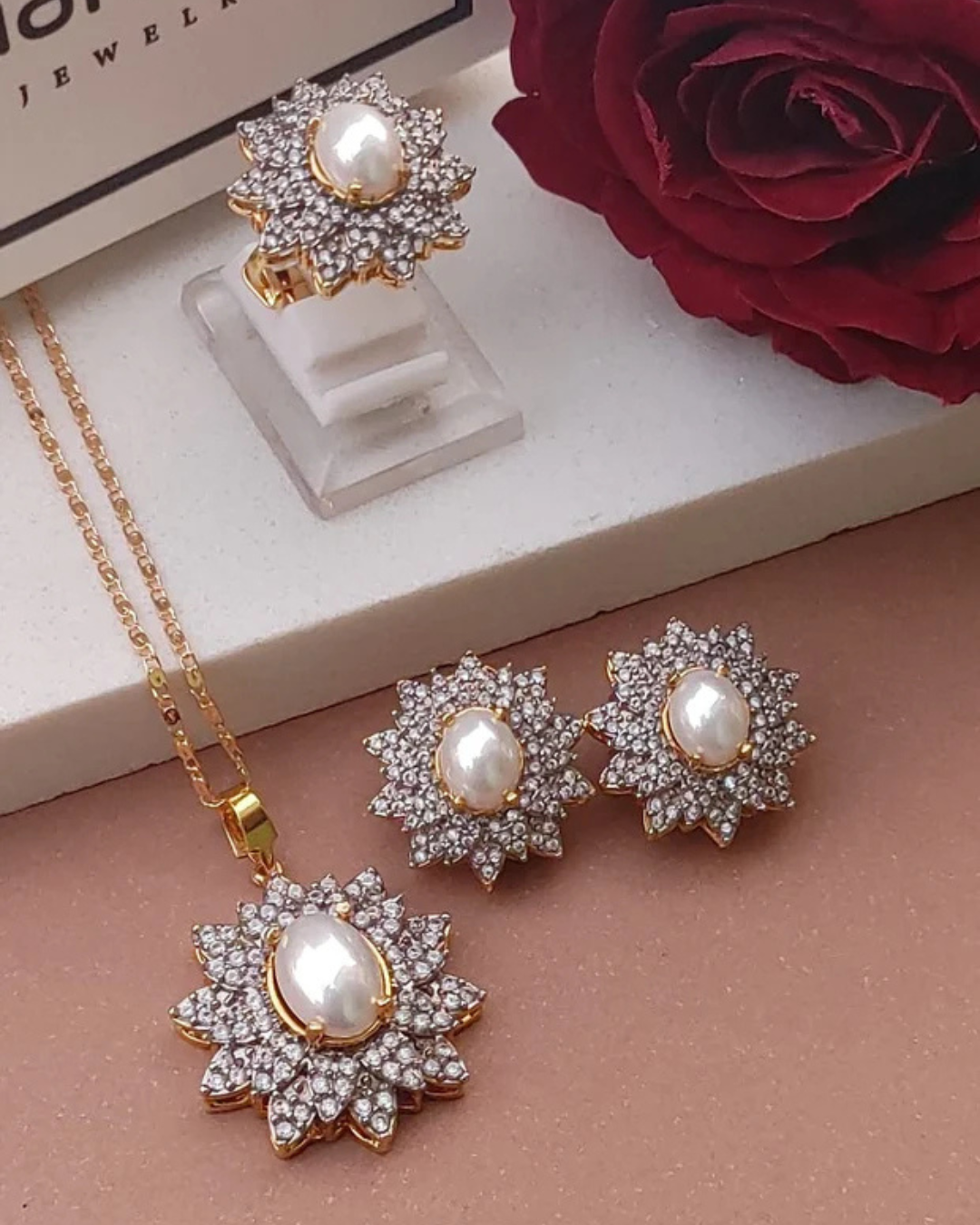 Jewelry set with necklace and earrings featuring pearls and zirconia stones on a beige surface.